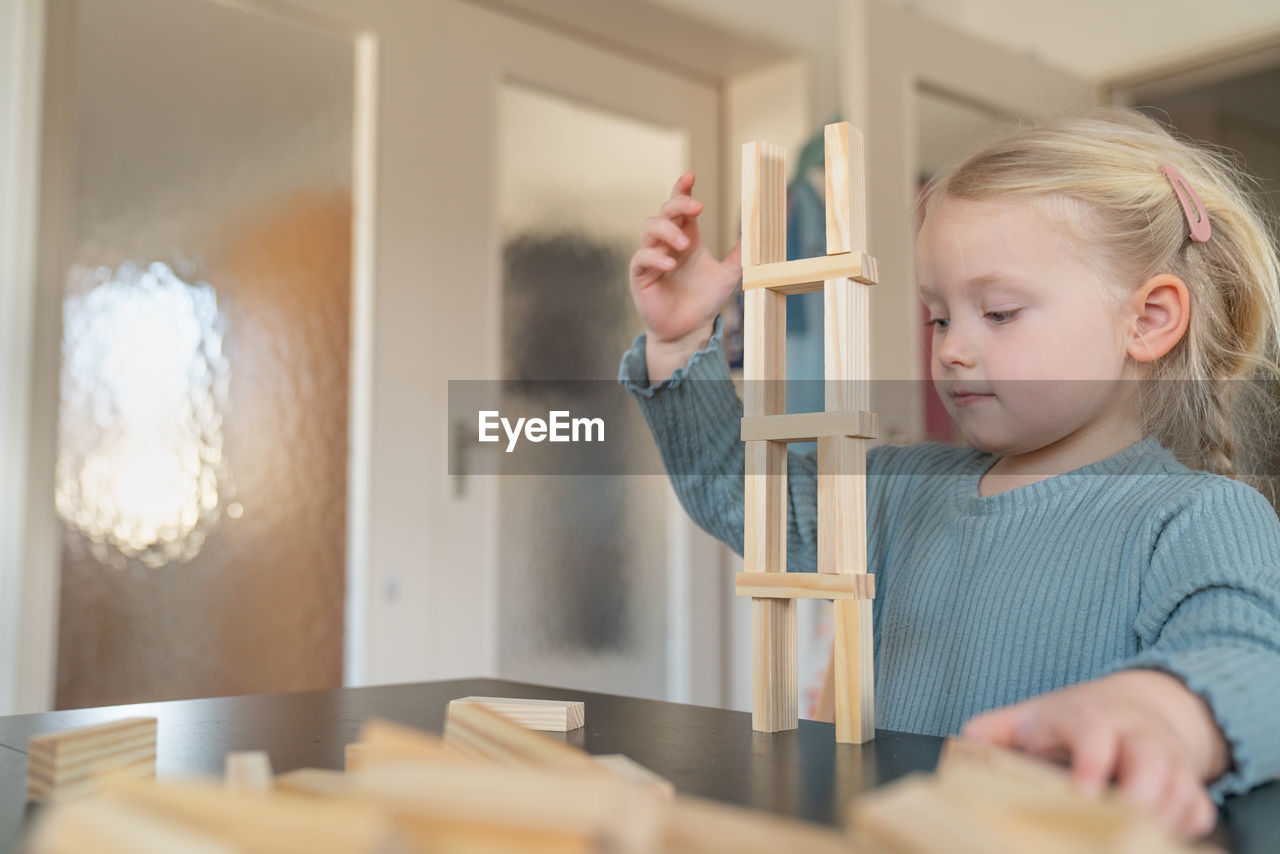 A toddler girl is building a house from wooden bricks