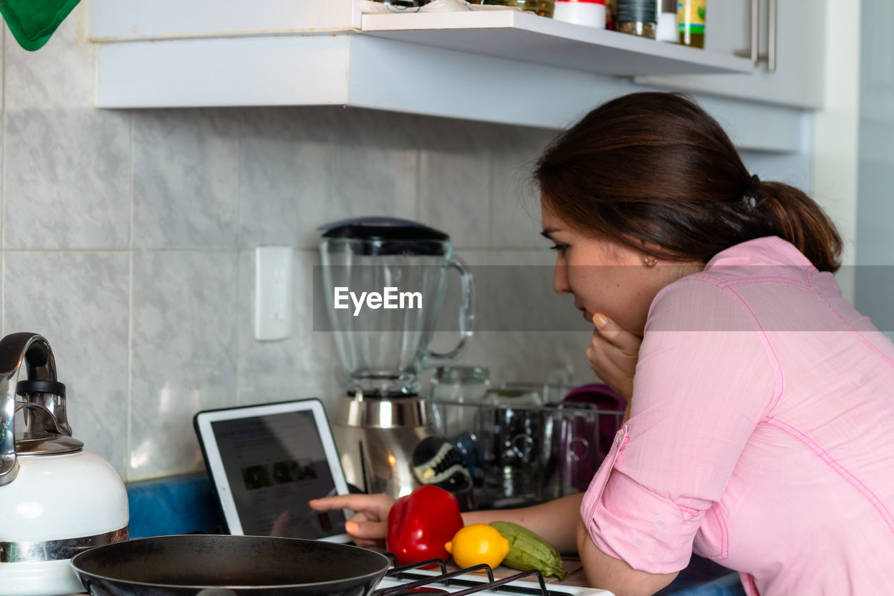 Woman reading recipe on digital tablet while preparing food at kitchen counter