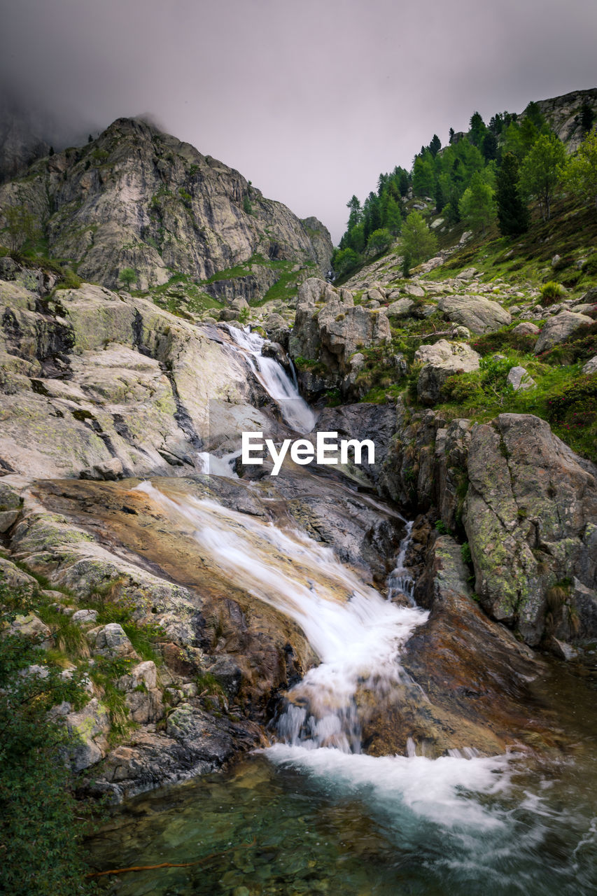 SCENIC VIEW OF WATERFALL ON MOUNTAIN AGAINST SKY