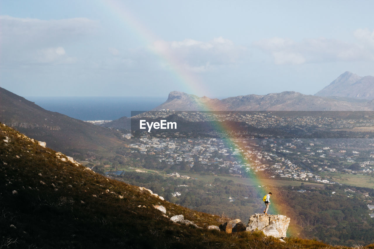 Man standing on mountain by rainbow against landscape