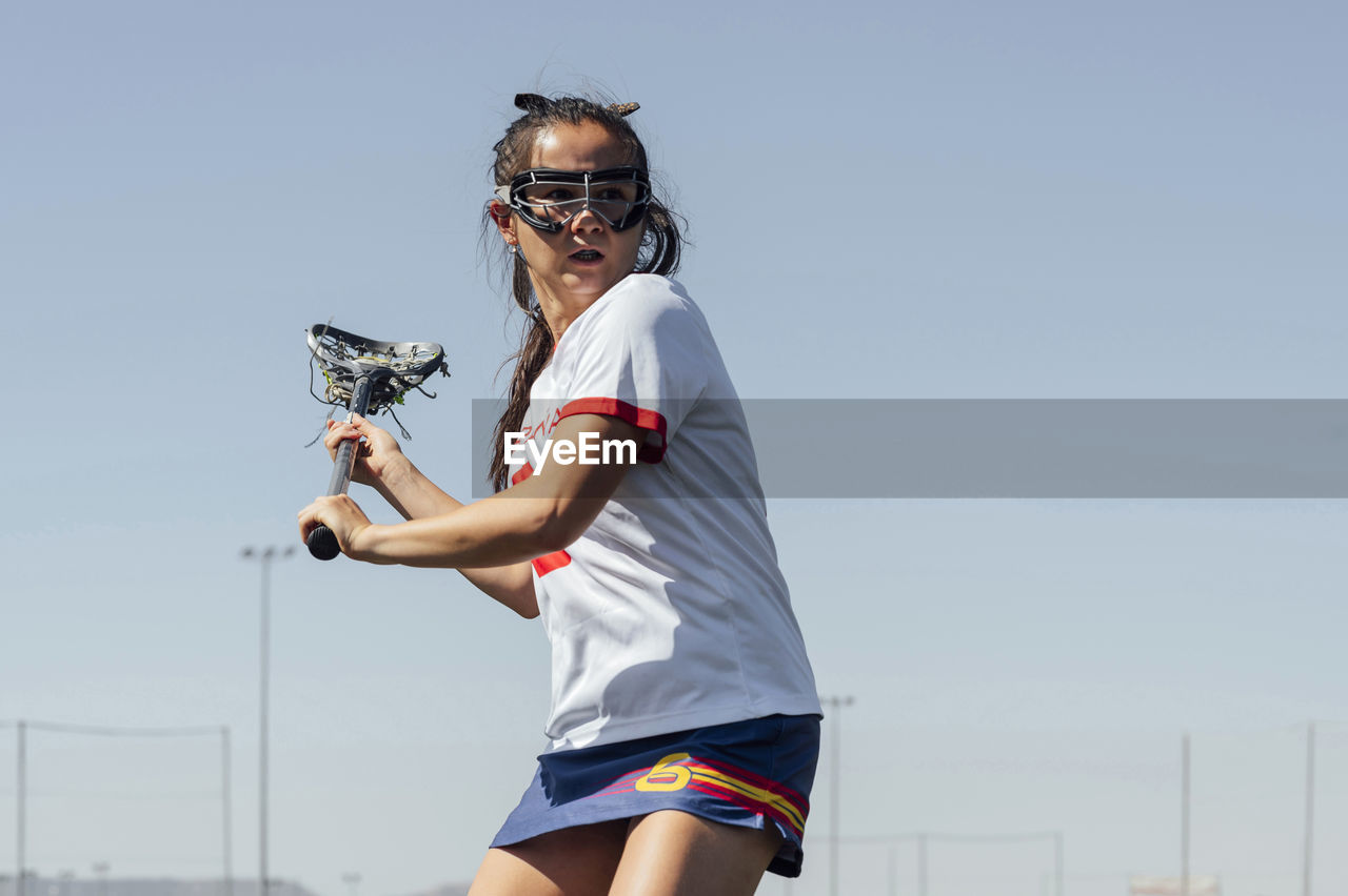 Determined player playing lacrosse in front of clear sky