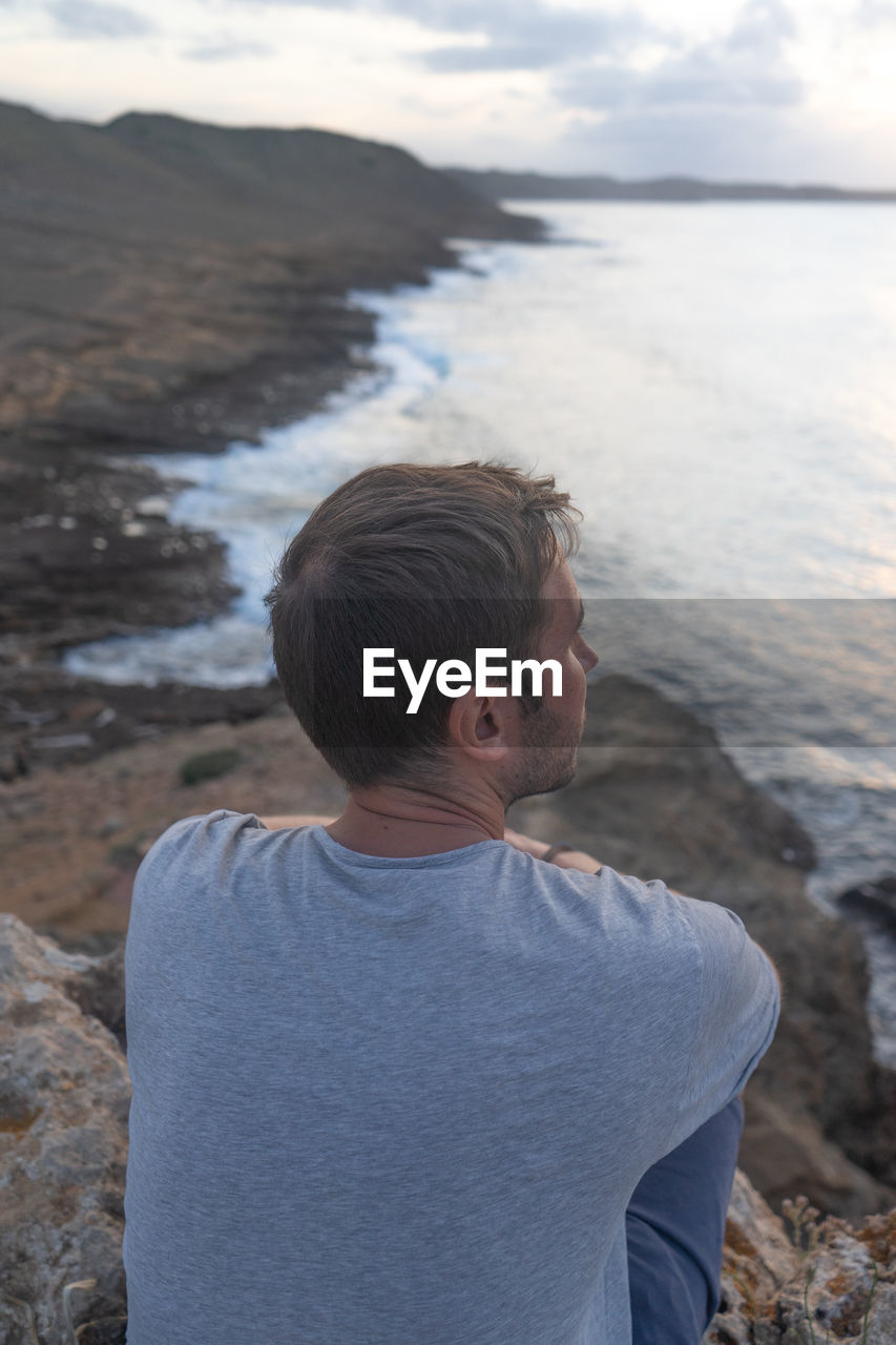 Side view of man looking at sea against sky during sunset