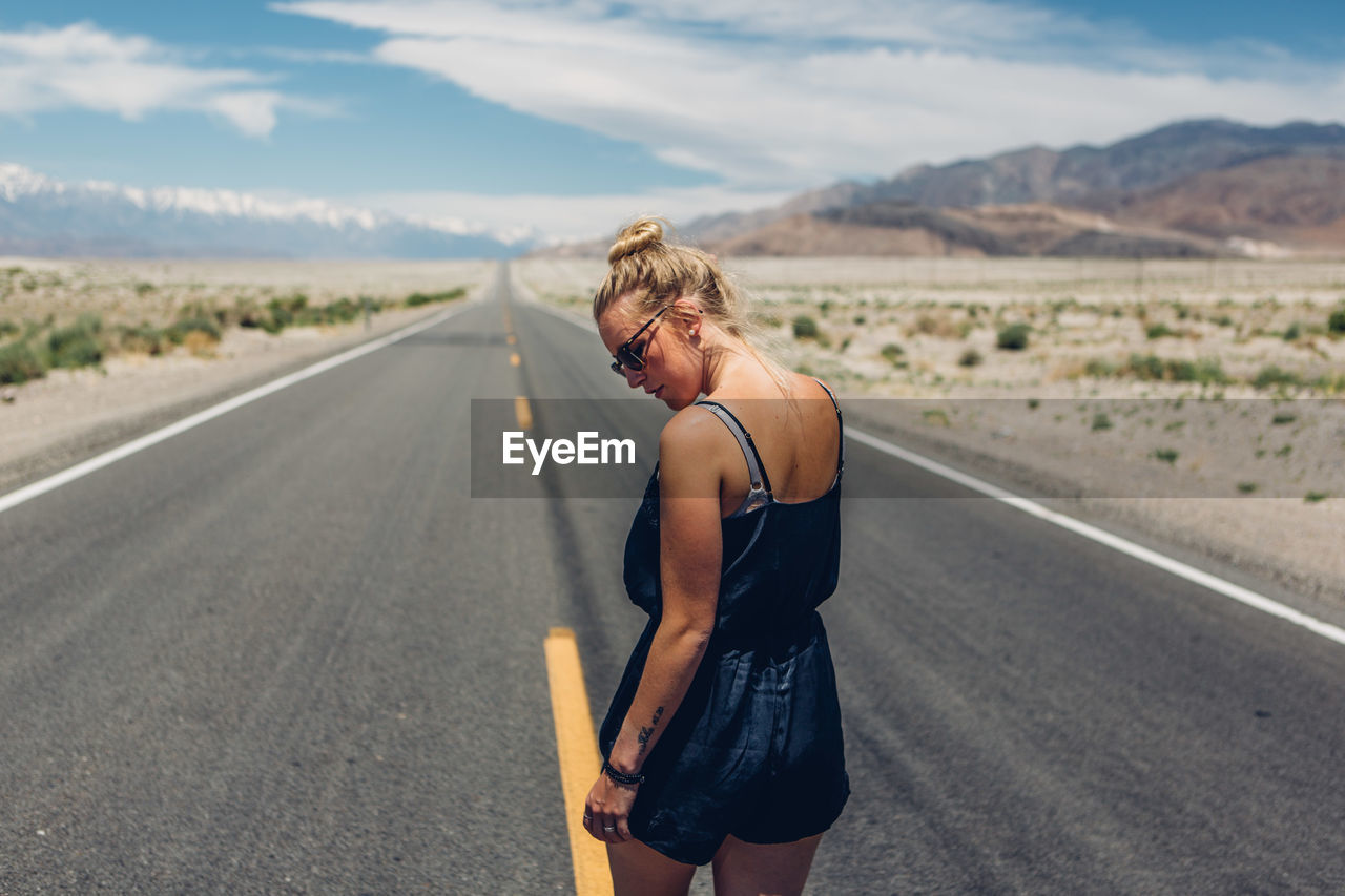 Rear view of young woman walking on road against sky