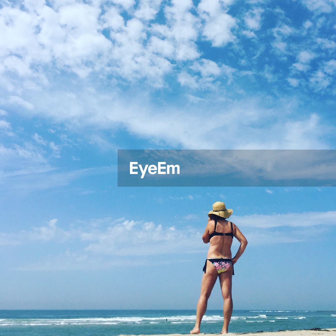 Rear view of woman wearing bikini standing on sea shore at beach against sky
