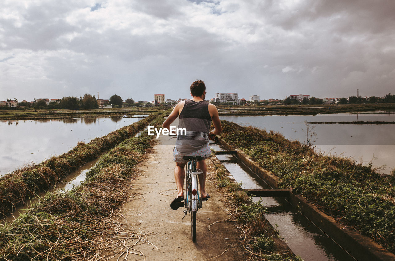 Rear view of man riding bicycle on water against sky