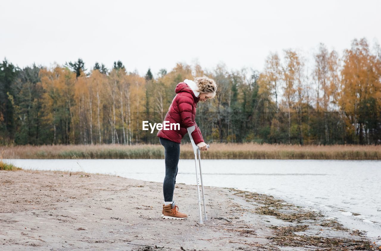 Injured woman stood at the beach with crutches looking thoughtful