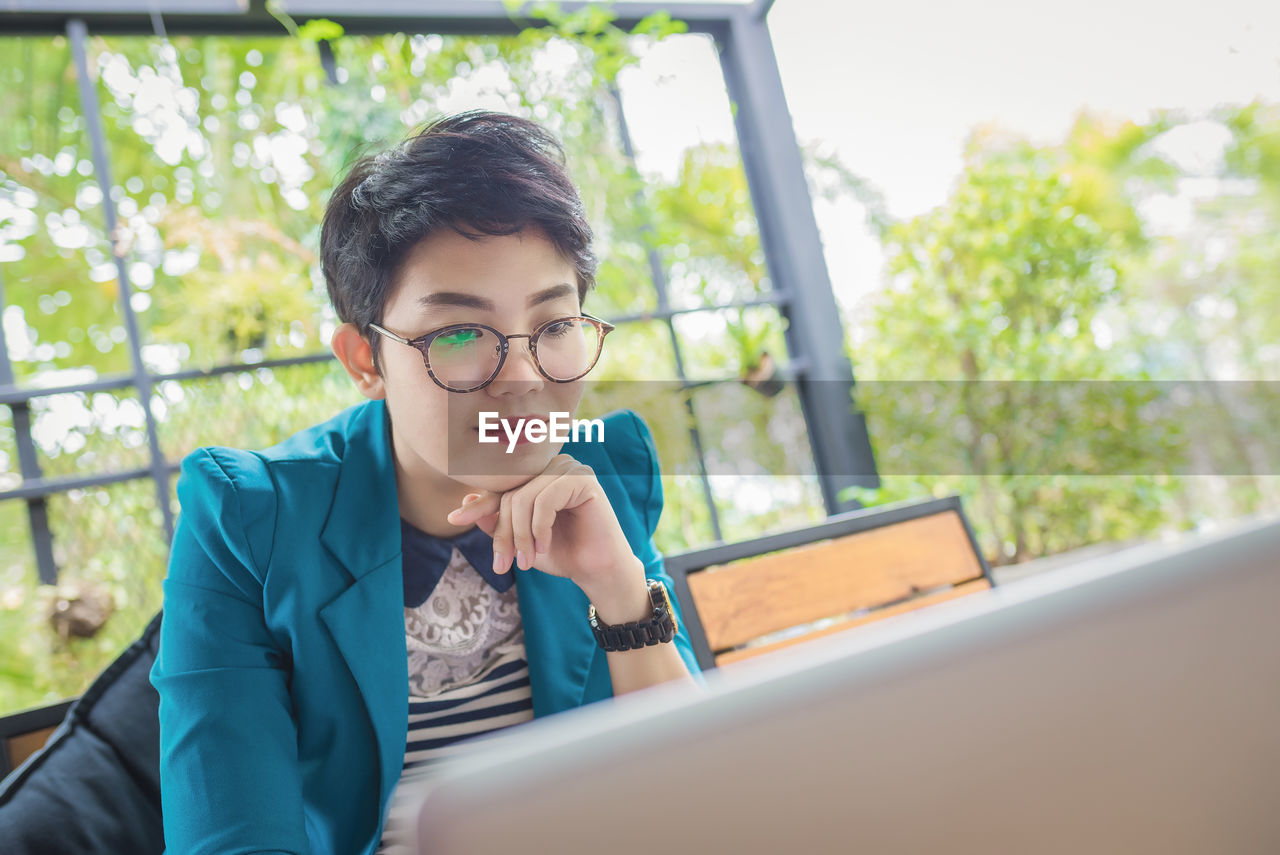 Young woman wearing eyeglasses while using laptop outdoors