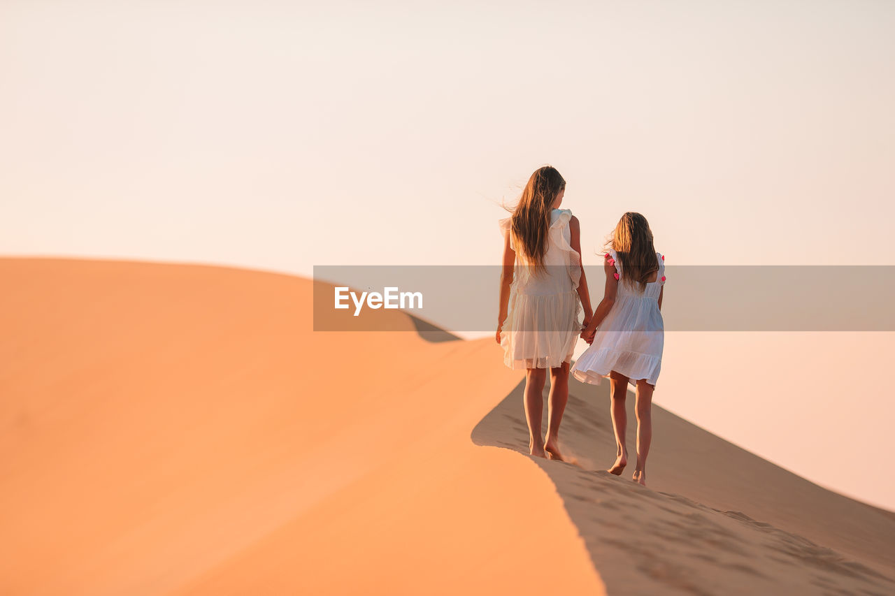 REAR VIEW OF WOMEN WALKING ON SAND DUNE IN DESERT