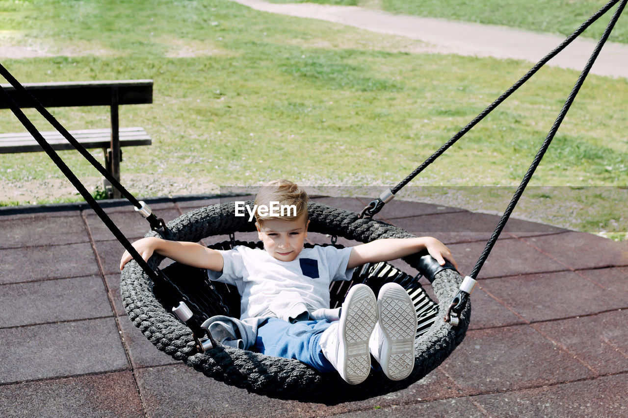 Smiling kid relaxing in a round swing and enjoying at the playground.