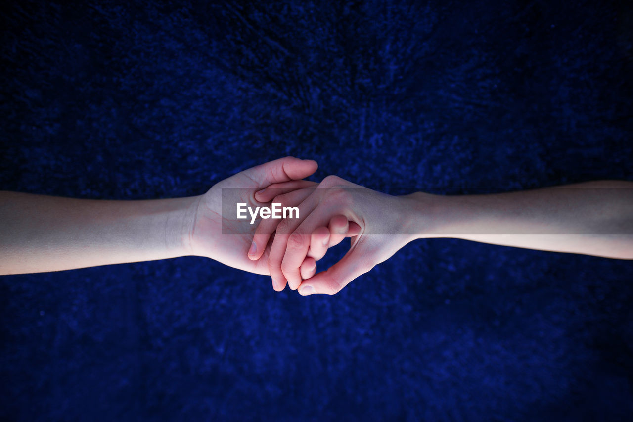 Cropped image of couple holding hands against blue background