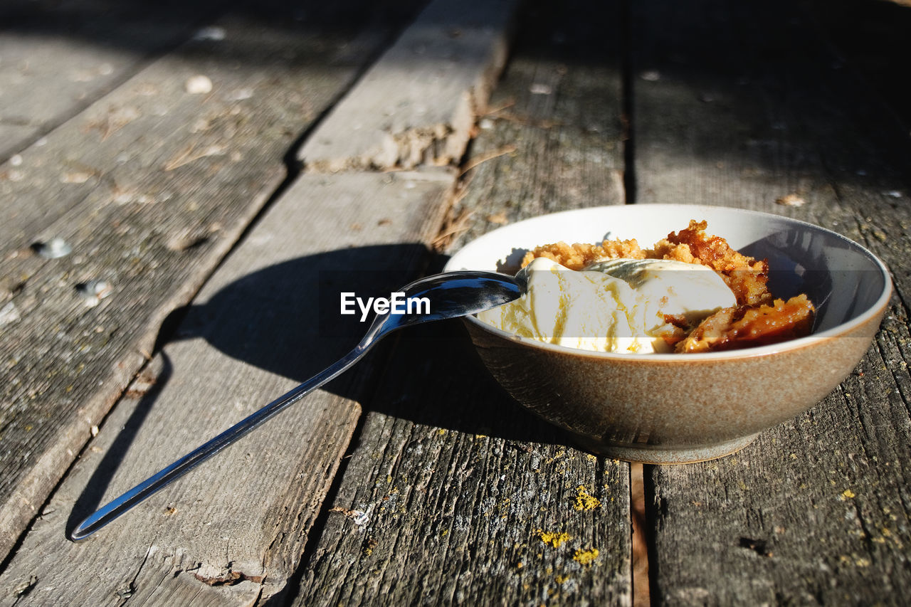A bowl of apple crumble with ice-cream over a wooden table. 