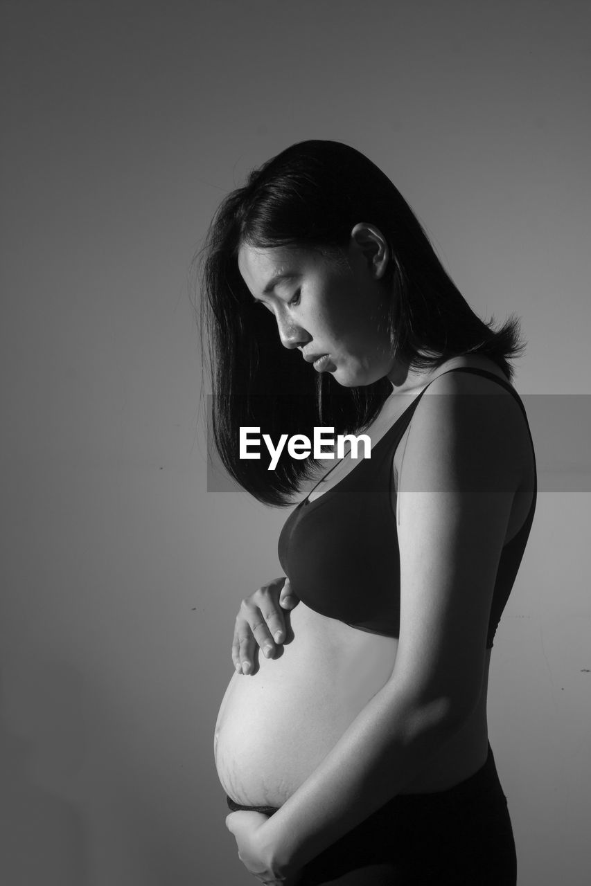 Side view of young pregnant woman against gray background