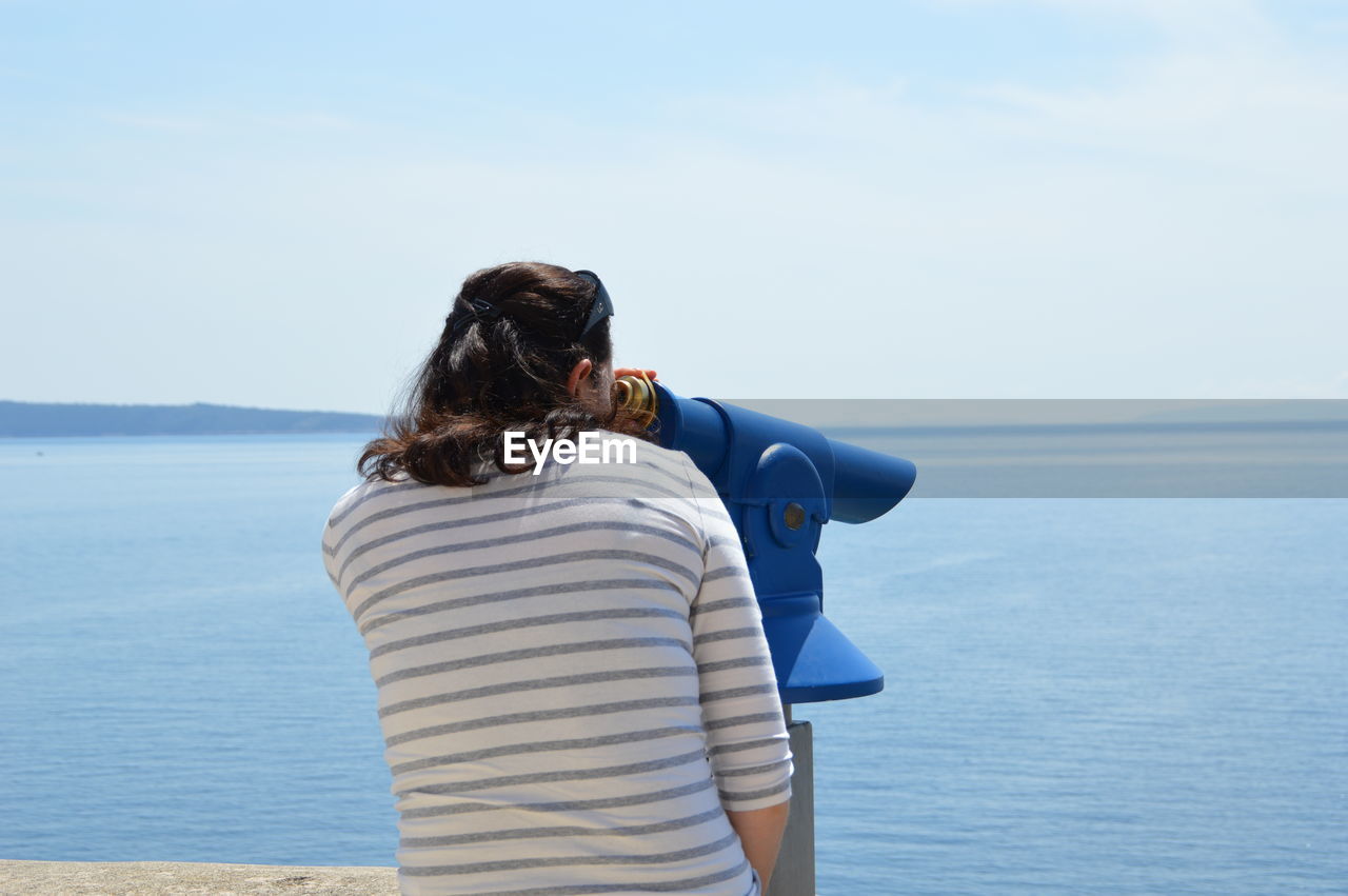 Rear view of woman looking through telescope against sea