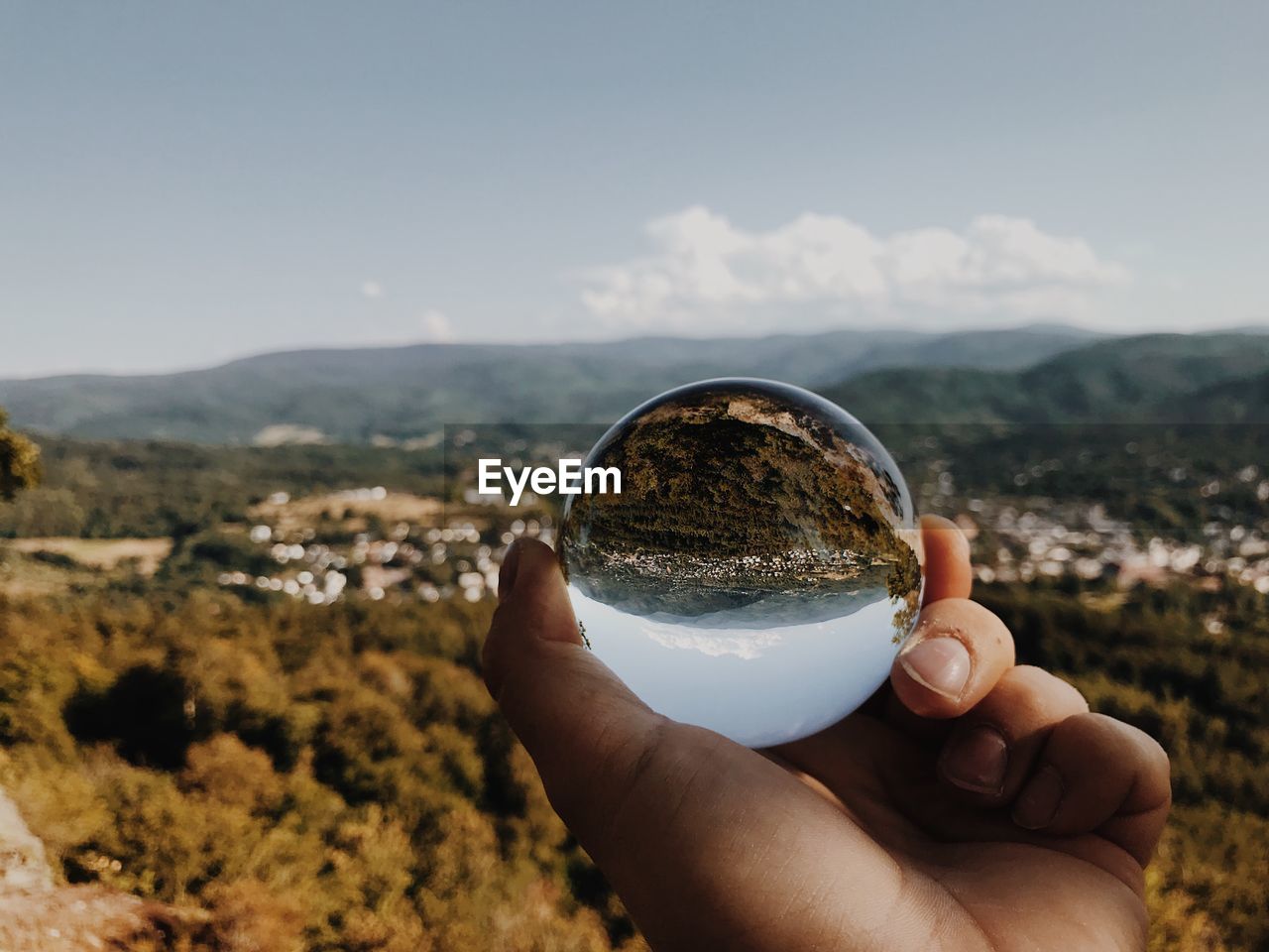 Cropped hand of person holding crystal ball on mountain against sky