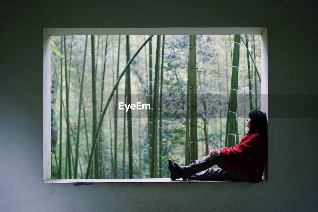 Side view of woman sitting on window