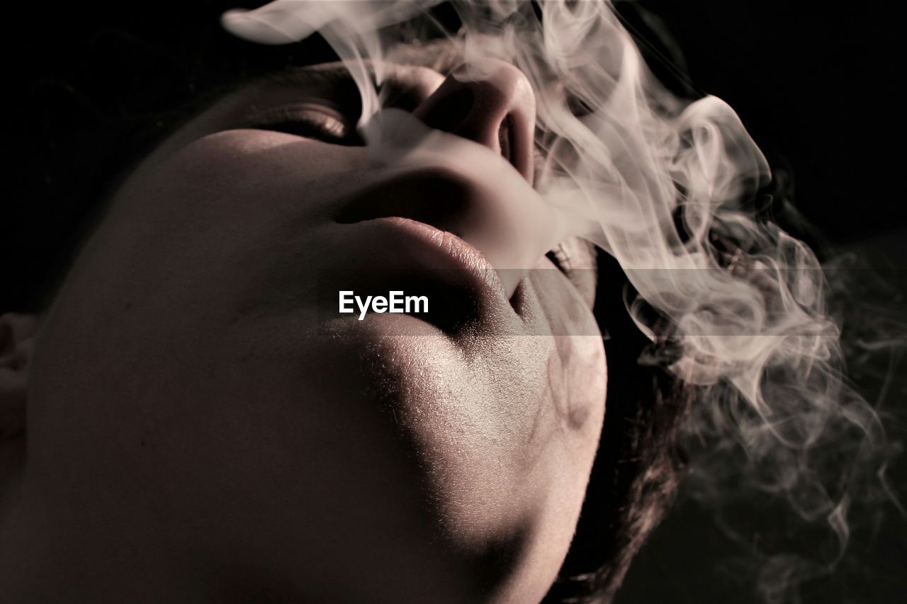 Close-up of man exhaling smoke against black background
