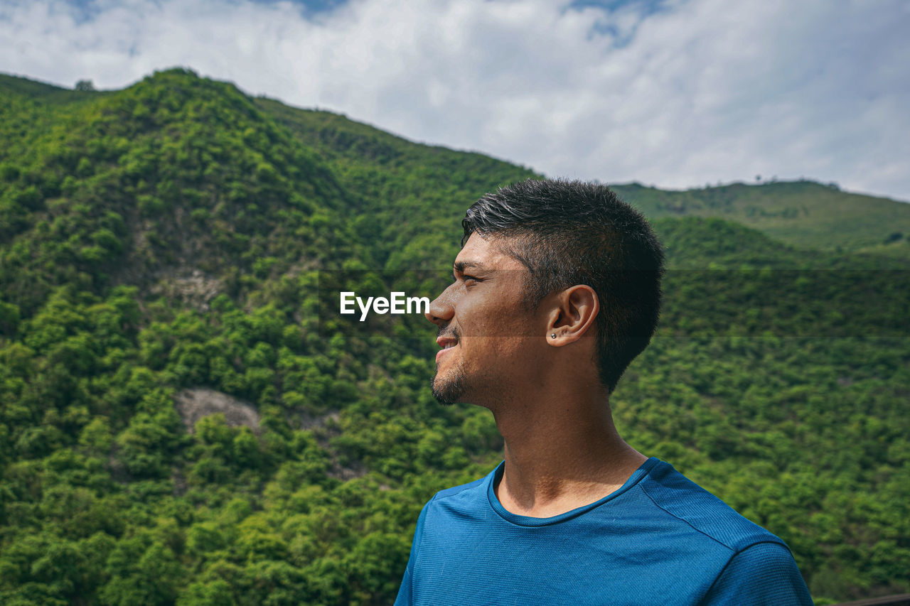 PORTRAIT OF YOUNG MAN LOOKING AWAY MOUNTAIN AGAINST MOUNTAINS