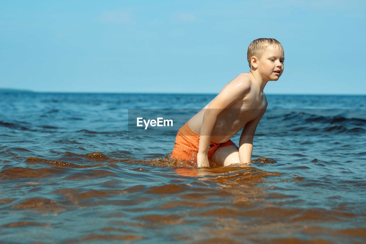 7-8 years old cute caucasian boy going out from the sea to the shore tired.