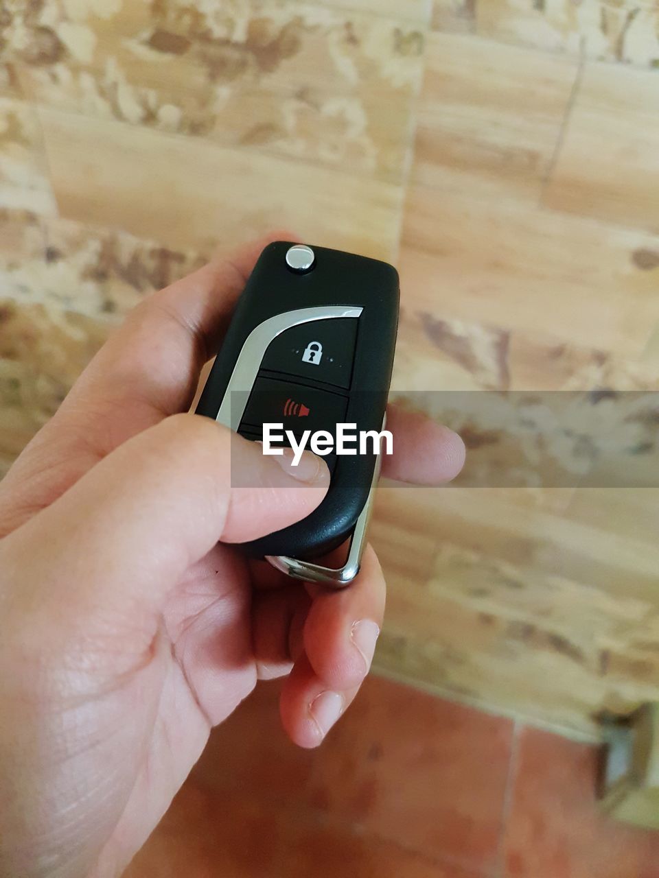 Cropped hand of person holding car key against wall
