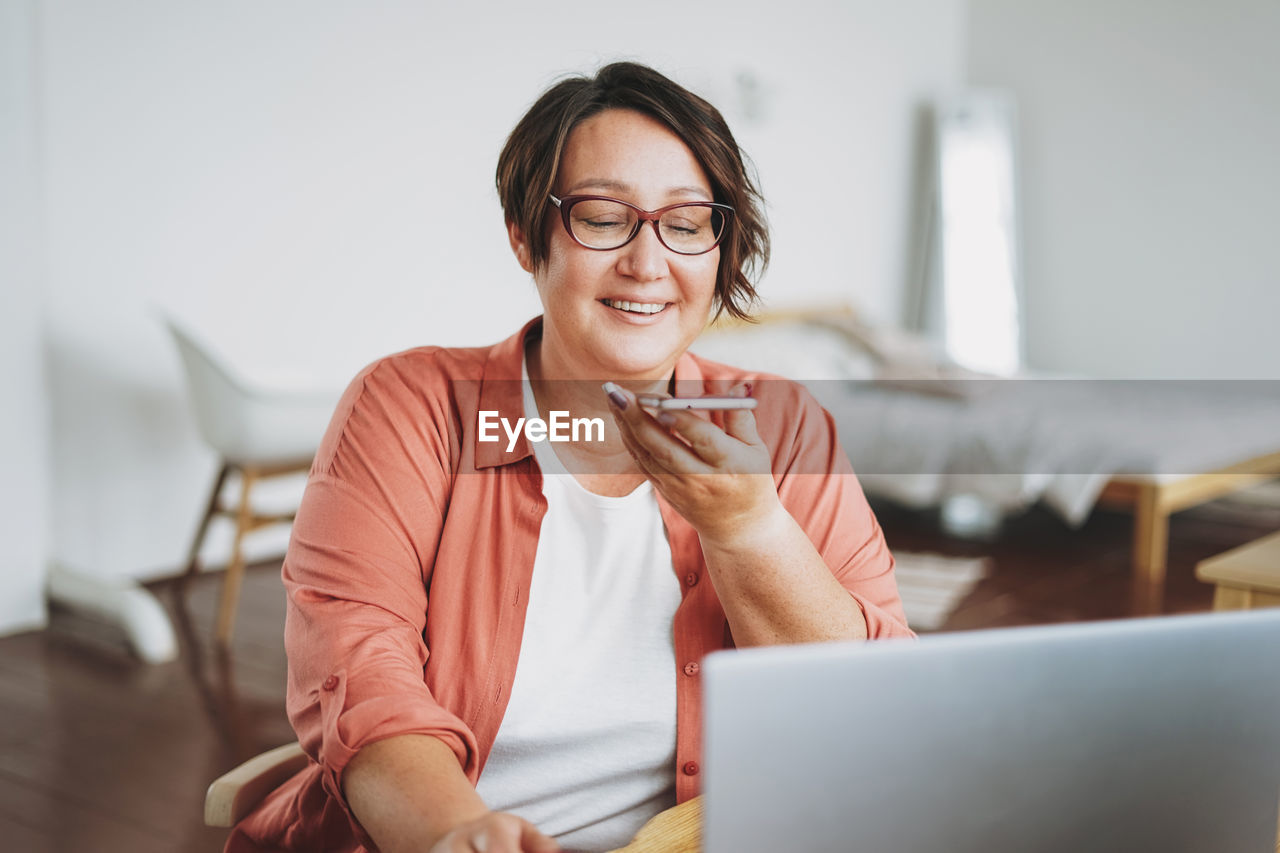 Adult charming brunette woman in glasses plus size body positive working with laptop at home