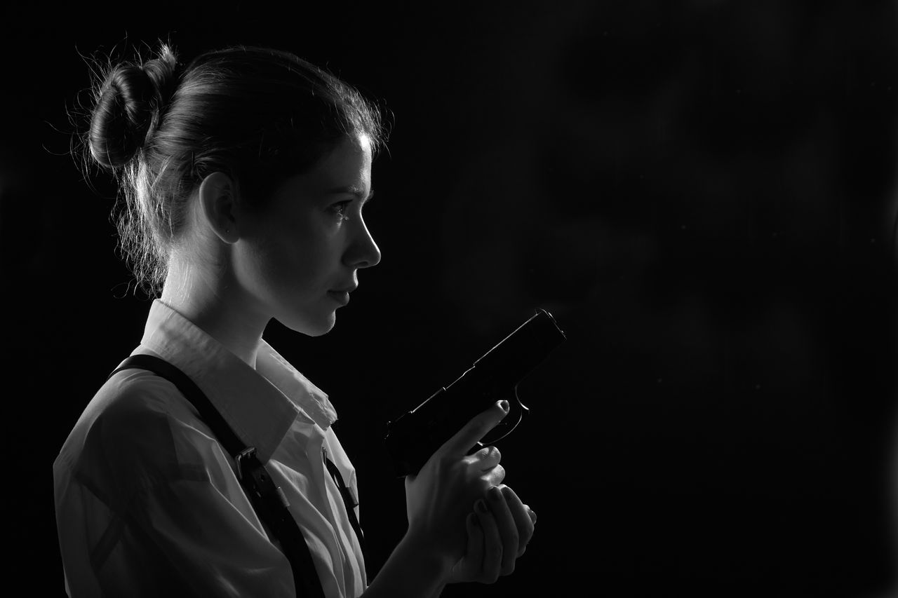 Young woman with gun in dark with back red light. profile silhouette view