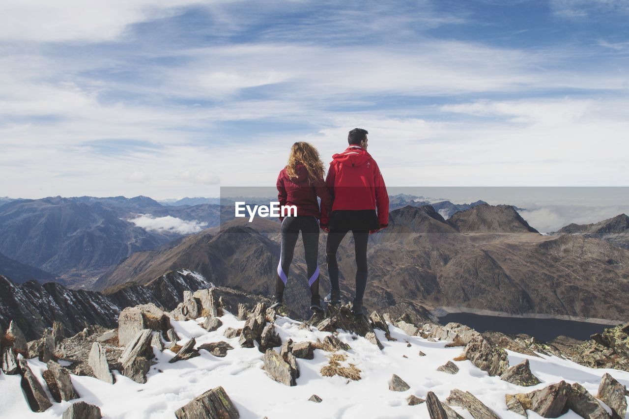 Rear view of couple standing on snowcapped mountains against sky