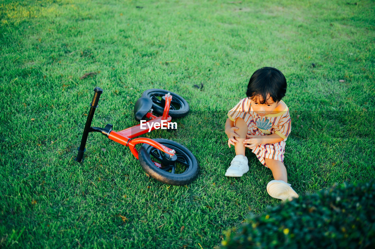 Boy sitting by cycle on grass