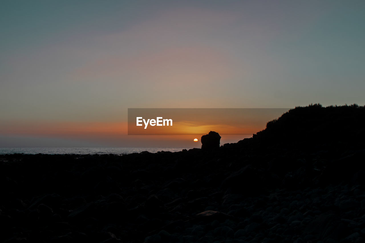 SILHOUETTE PERSON STANDING ON LAND DURING SUNSET
