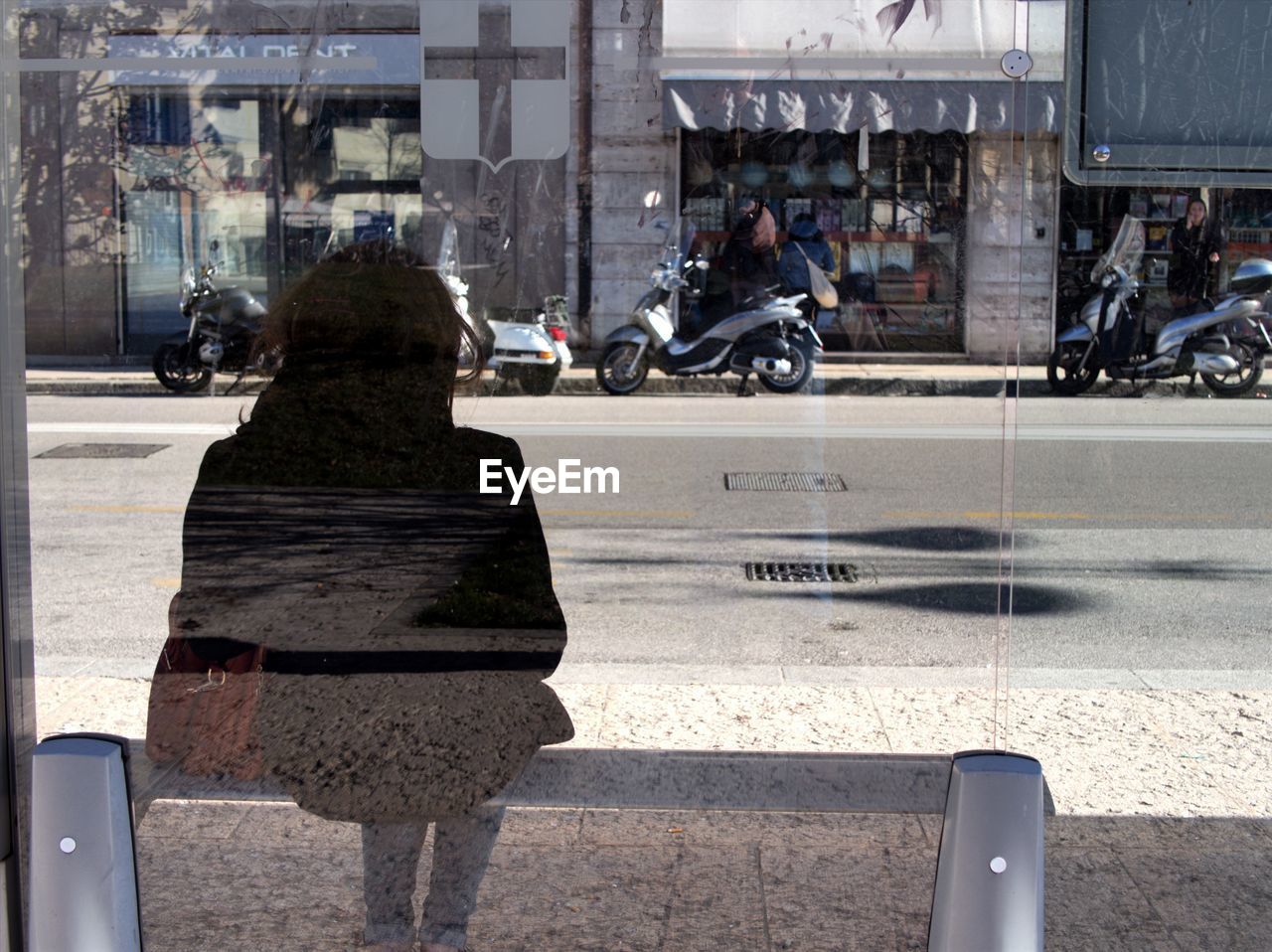 Reflection of woman on glass while sitting at bus stop