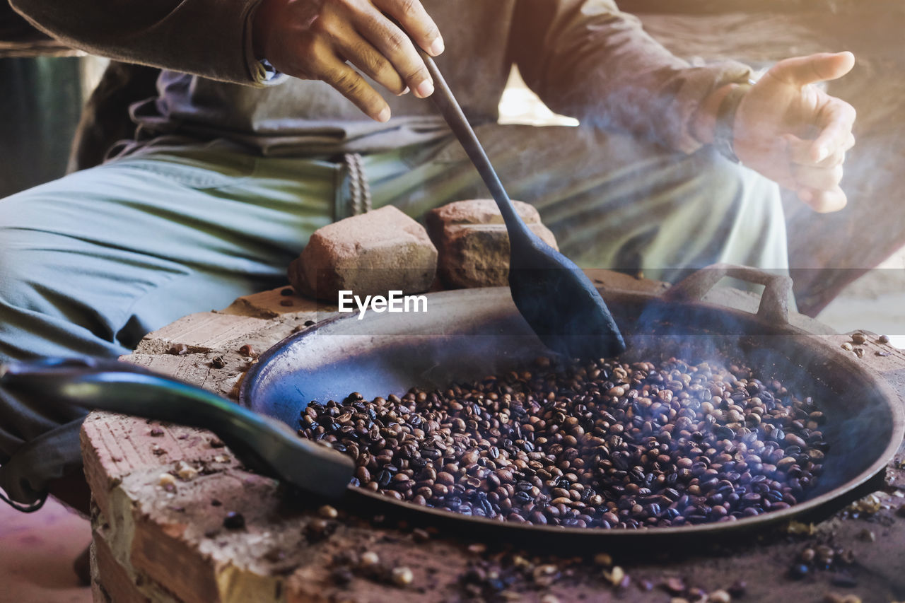 Asian men are sitting roasting coffee beans in a pan on an antique stove