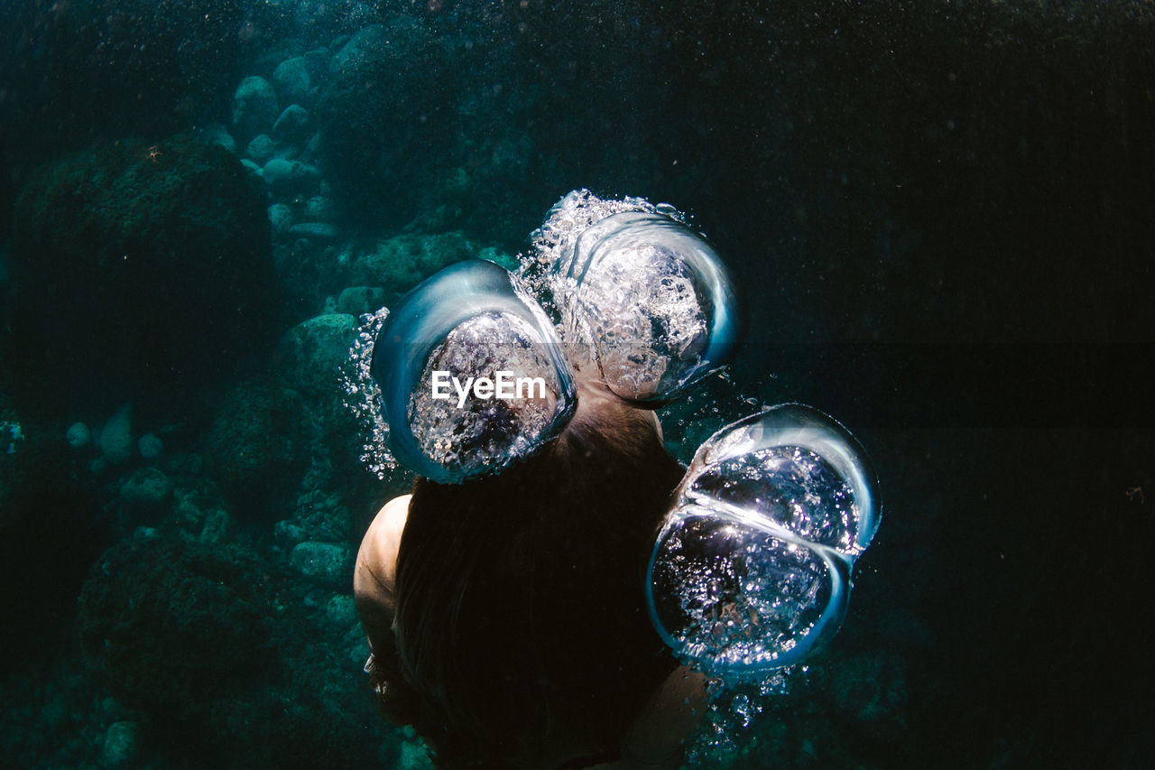 High angle of woman swimming underwater in sea amidst bubbles