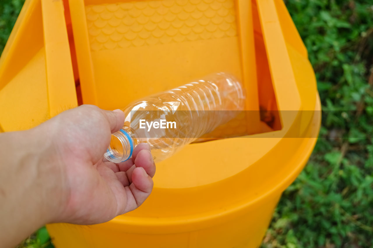 Close-up of hand throwing plastic bottle into garbage bin