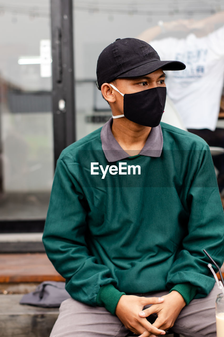 Young man wearing mask sitting outdoors