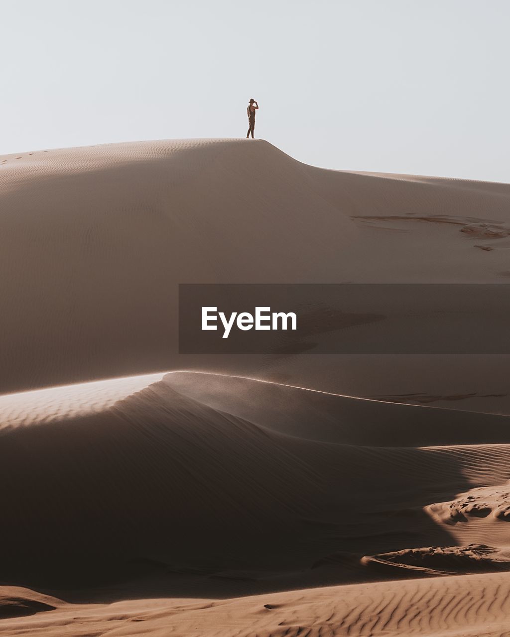 Distant view of man standing on sand dune at desert against sky