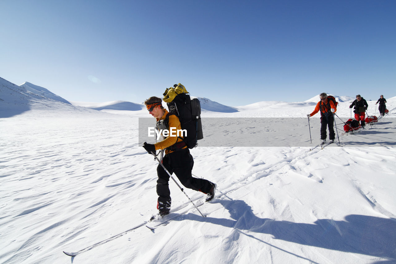 PEOPLE SKIING ON SNOWCAPPED MOUNTAINS AGAINST SKY