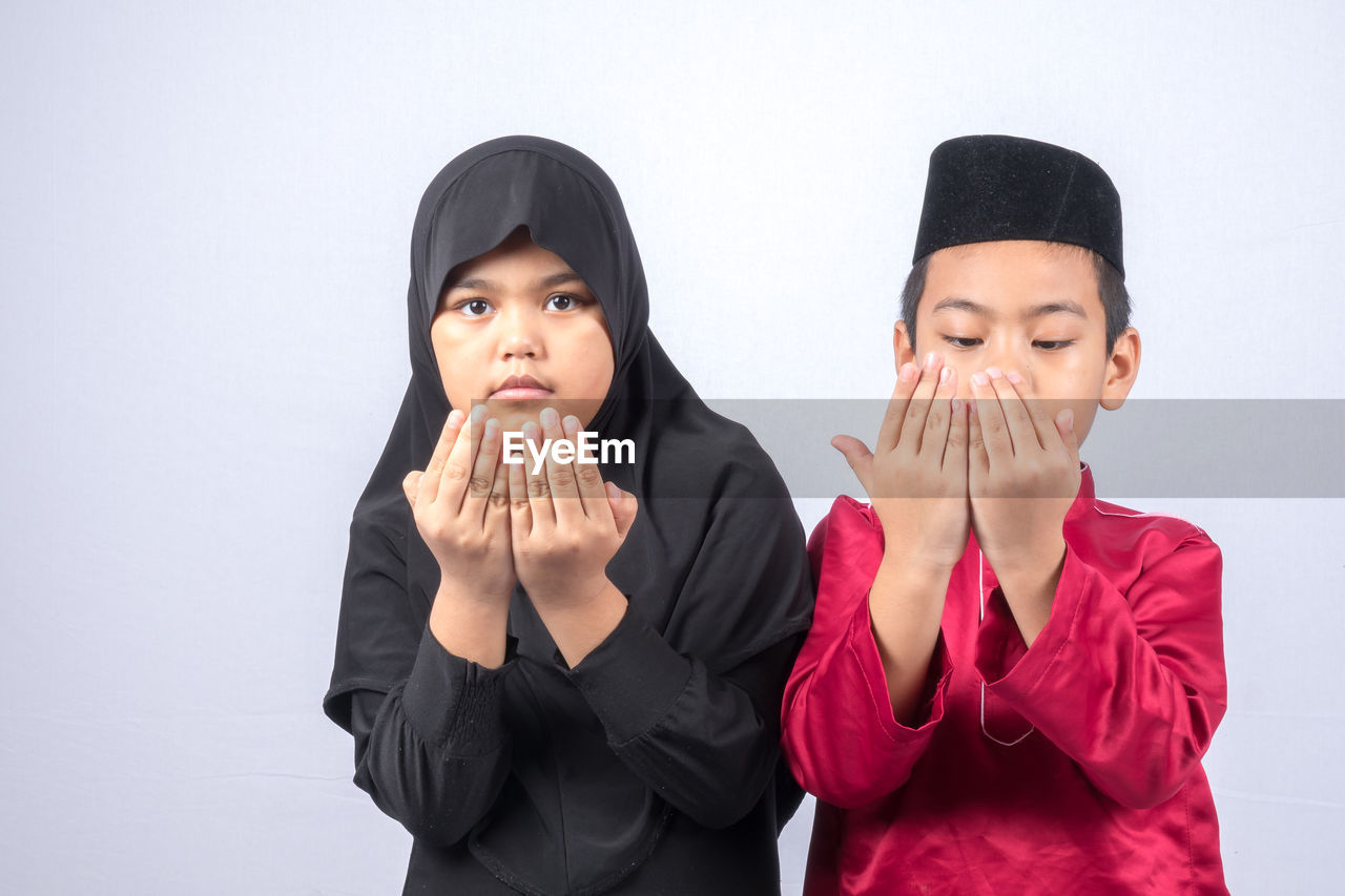 Siblings in traditional clothes praying against white background