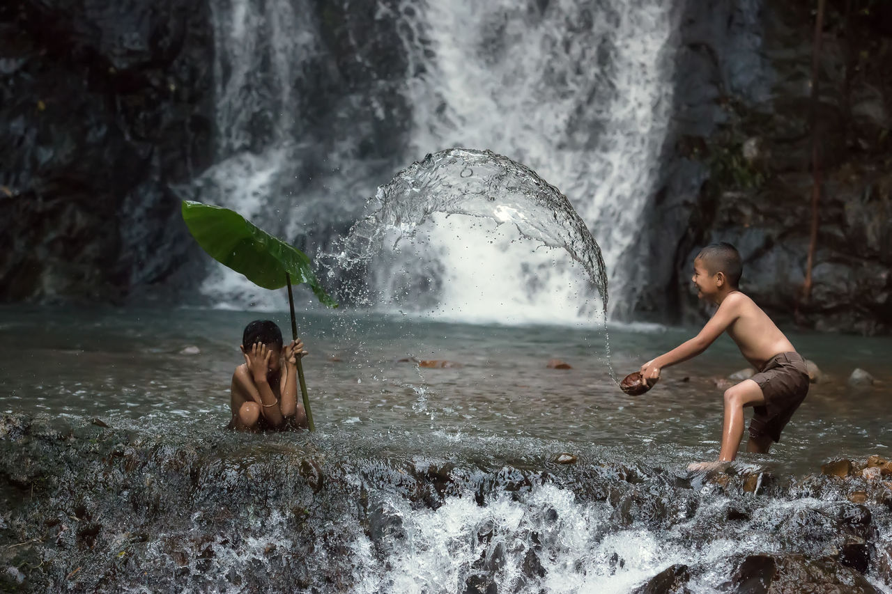 Shirtless boys playing in stream against waterfall
