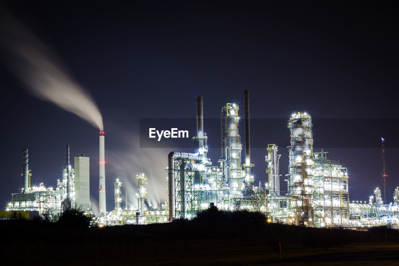 Illuminated petrochemical plant against sky at night