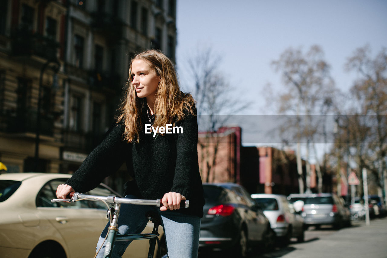Smiling young woman with bicycle on street in city