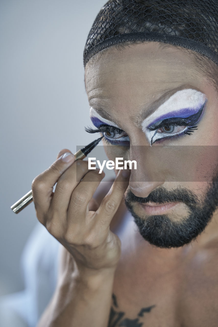 Shirtless man applying eyeliner at home