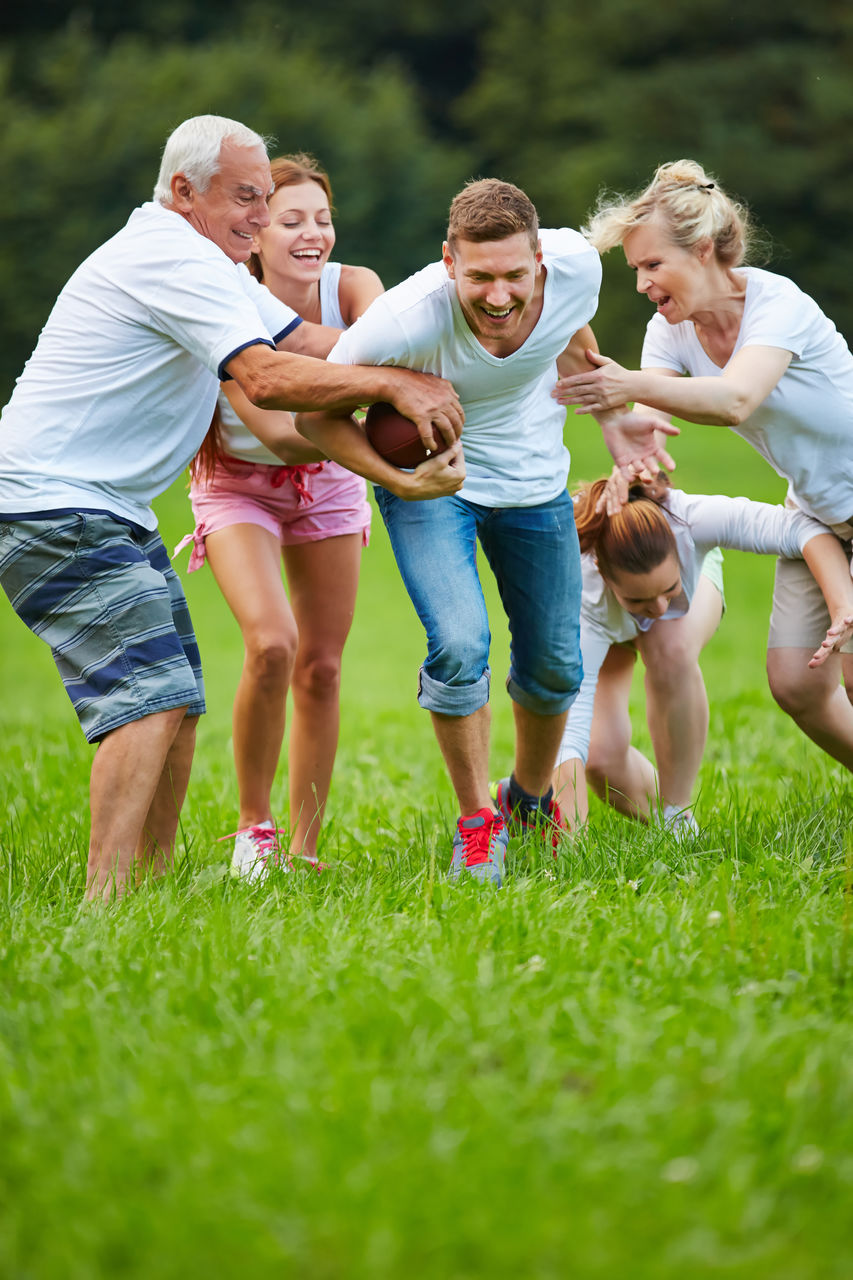 Cheerful friends playing american football at park