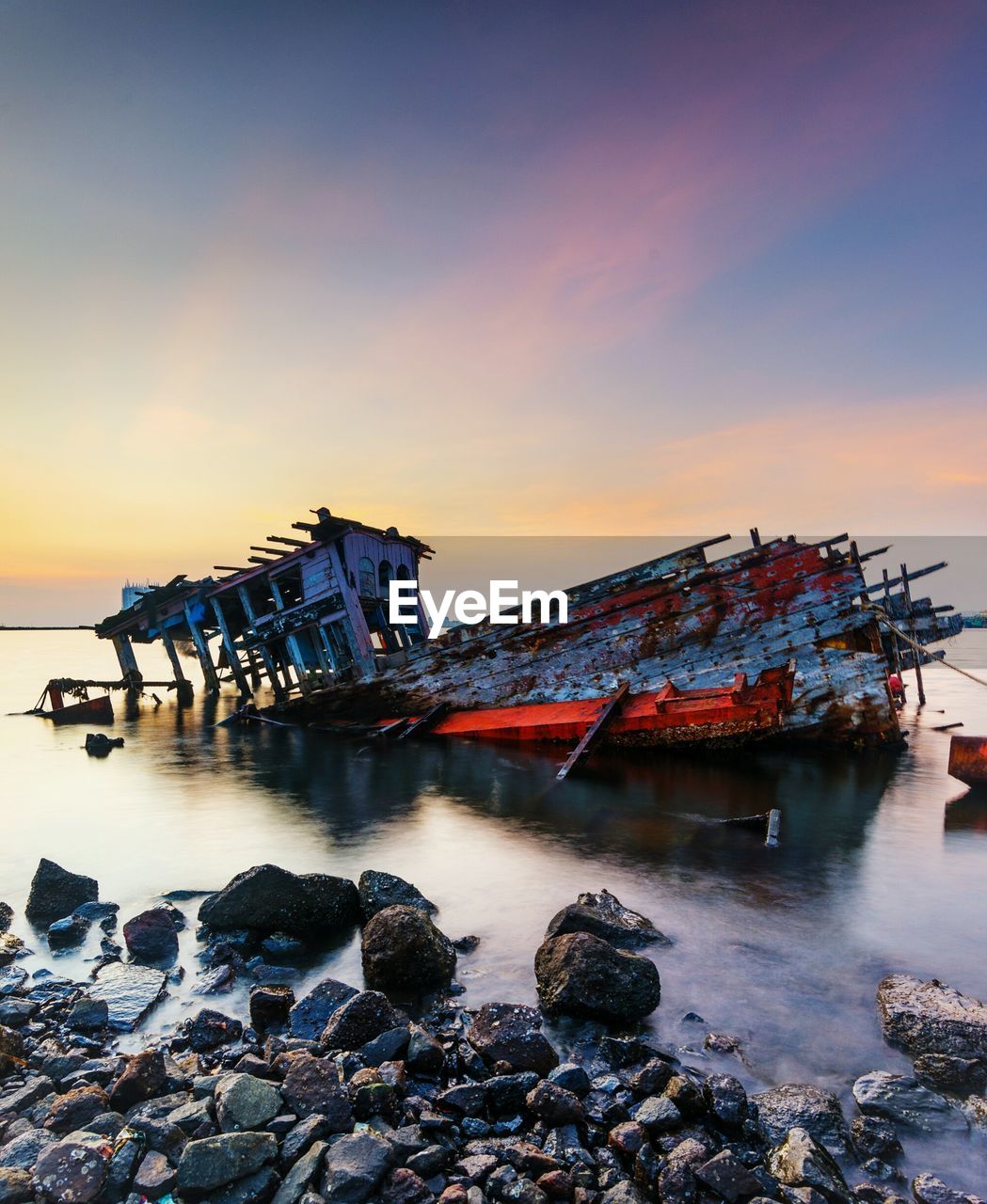 Abandoned boat sinking in sea against sky during sunset
