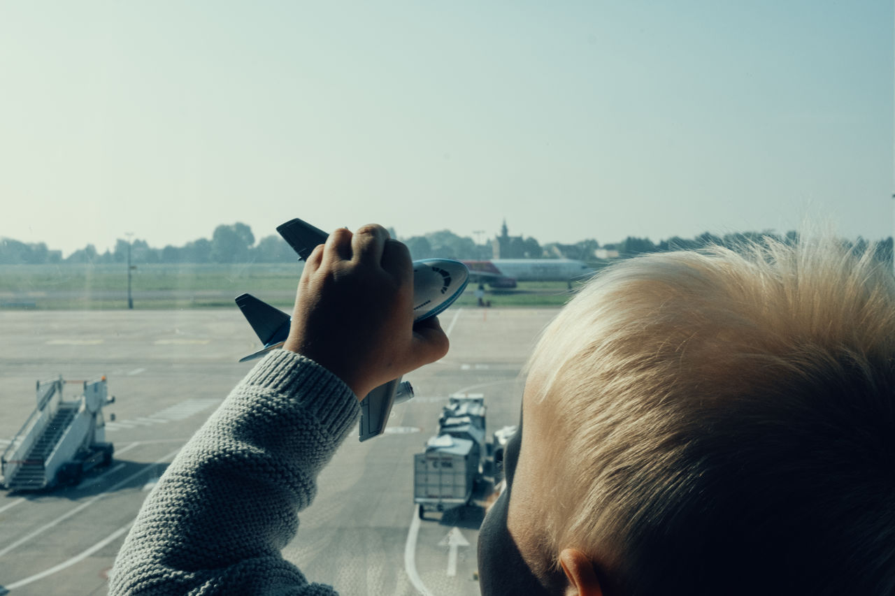Close-up of boy holding toy airplane on glass window at airport