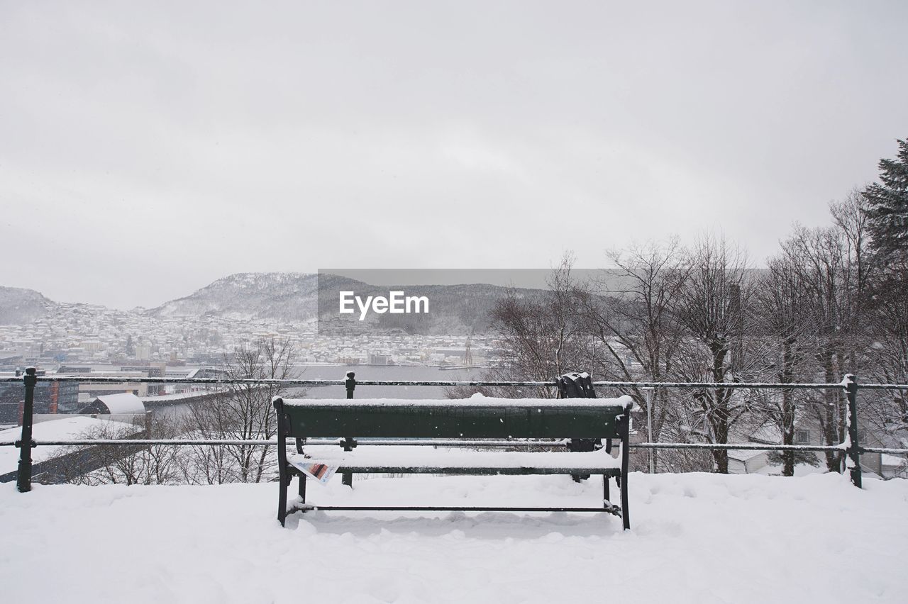 Empty frozen bench against sky