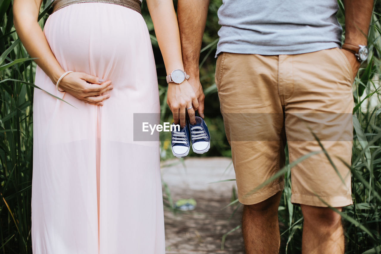 Midsection of pregnant woman with husband holding baby booties outdoors