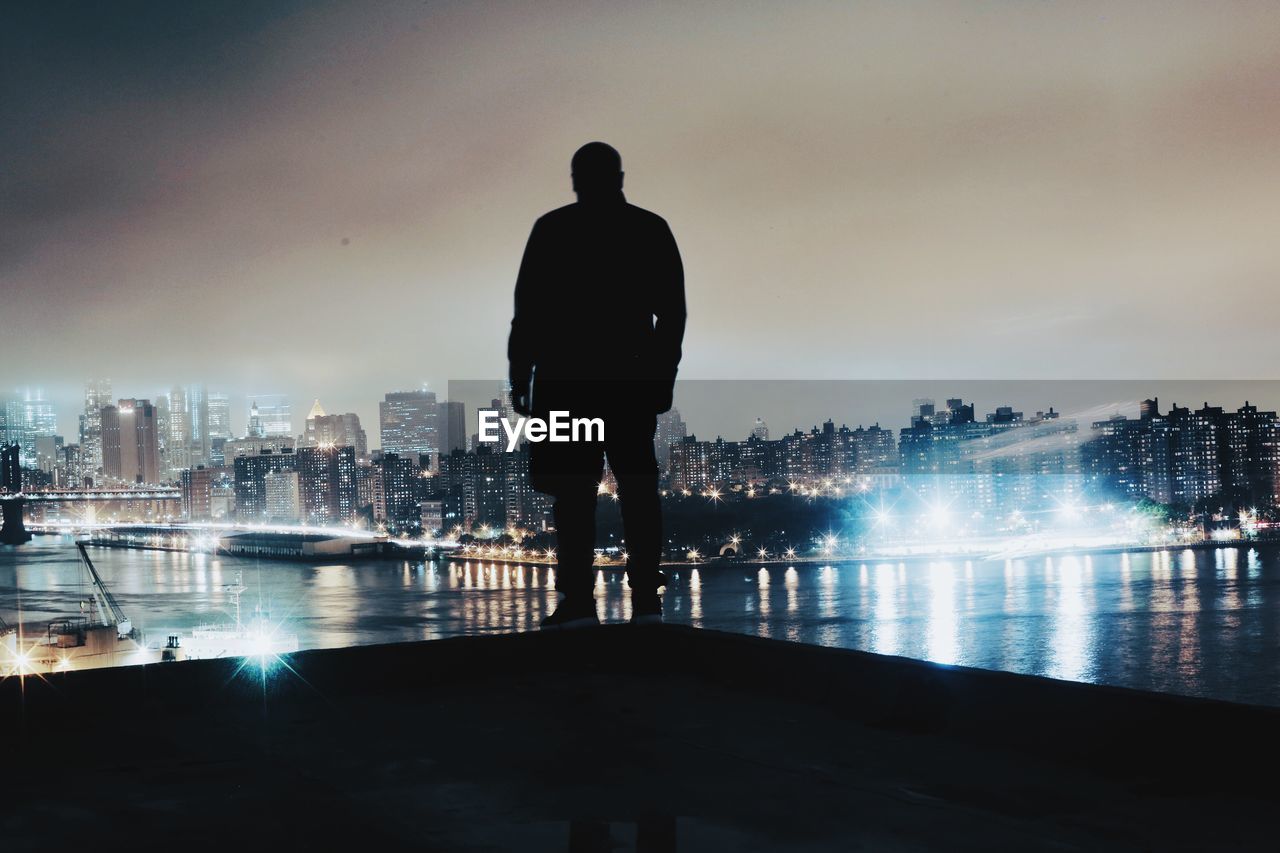 Rear view of silhouette of man with cityscape in background