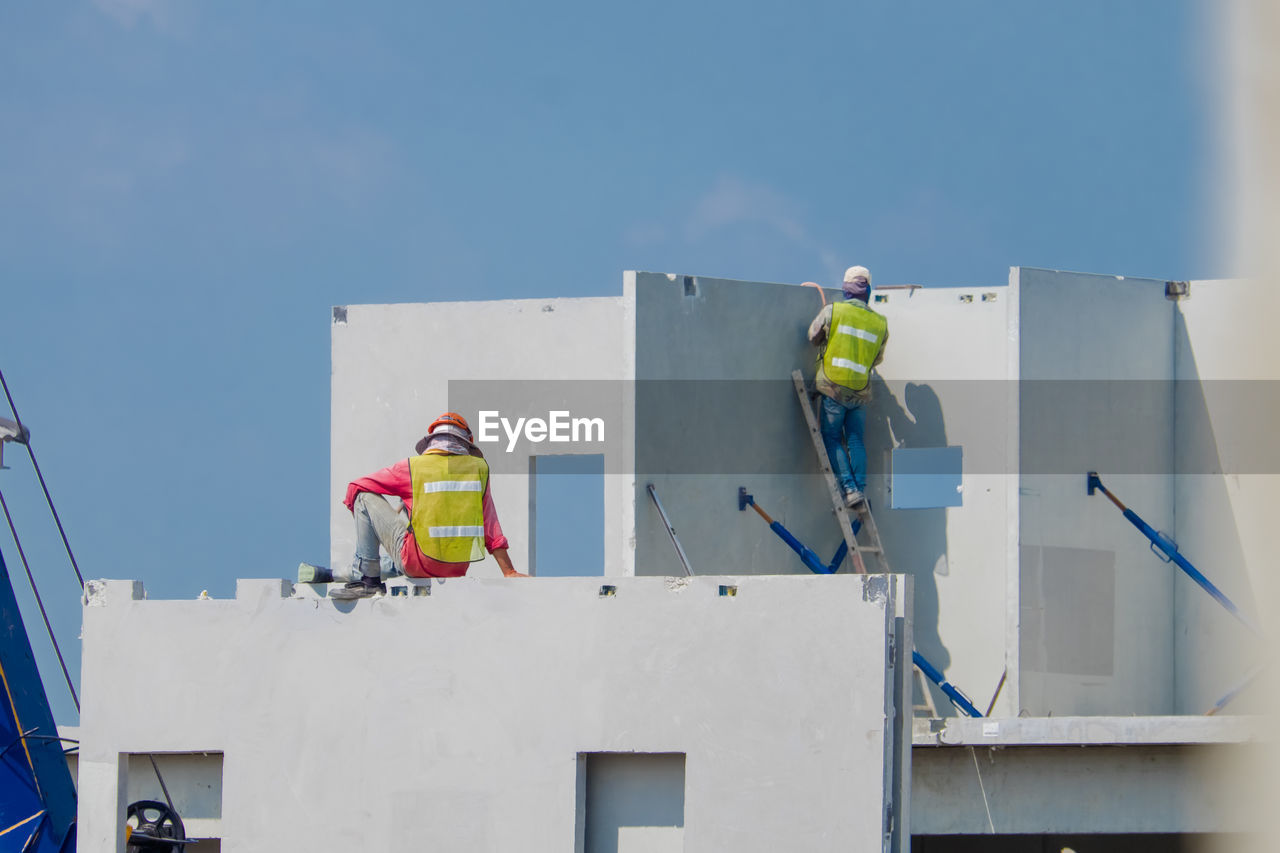 LOW ANGLE VIEW OF MEN WORKING ON BUILDING AGAINST SKY