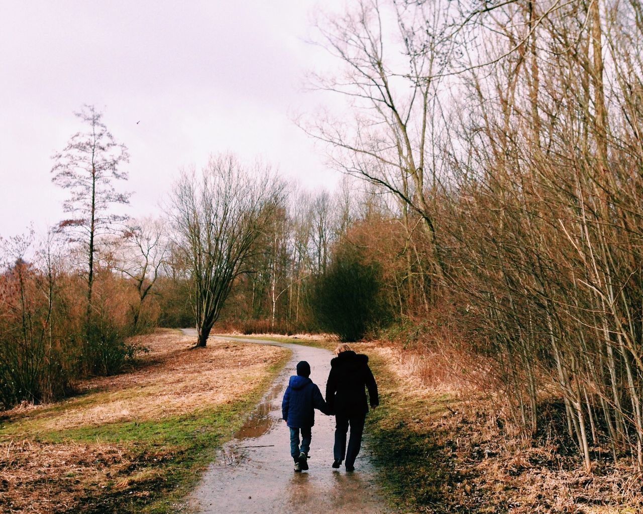 Rear view of man and boy walking on wet footpath by bare trees