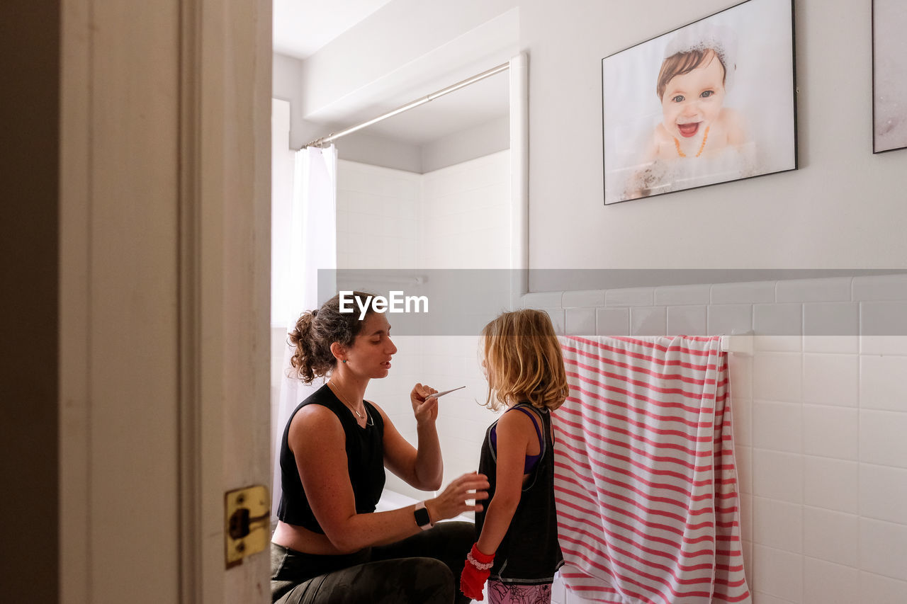 Mother and daughter in bathroom reading temperature on thermometer
