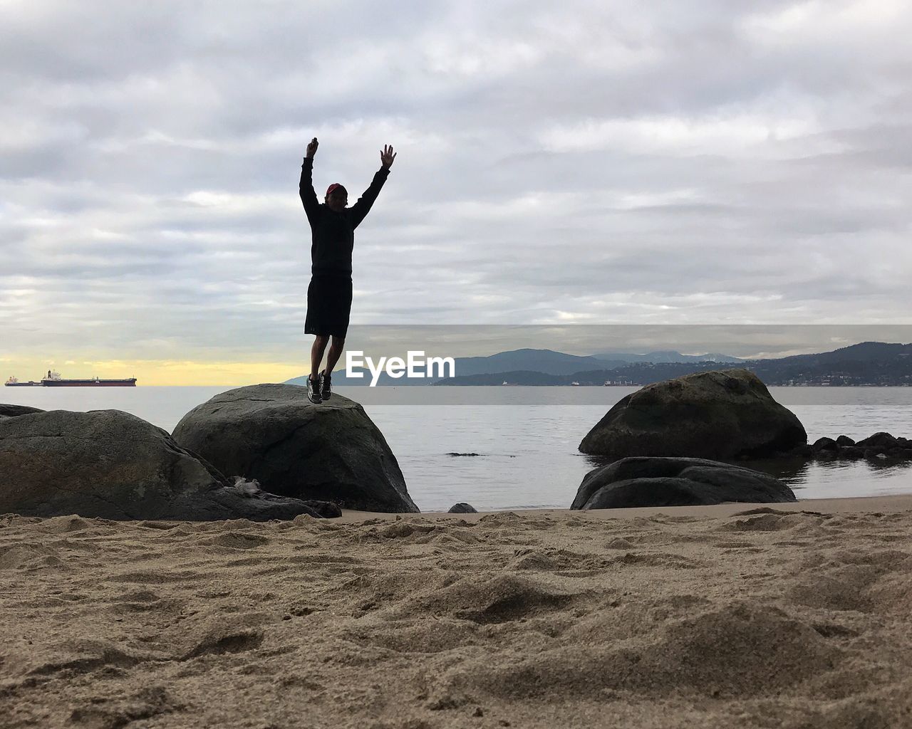 WOMAN JUMPING ON ROCK AT BEACH